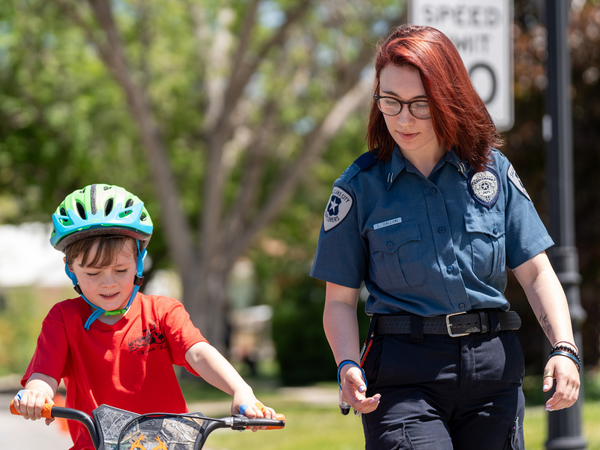 Police officer walking along side a child on a bike. 
